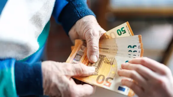 Eine ältere Frau gibt einer Person an der Haustür Geldscheine aus ihrem Portemonnaie.