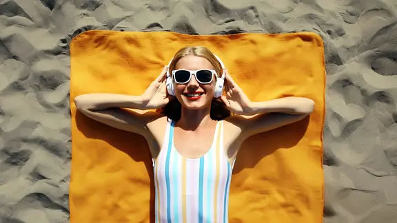 Junge Frau, am Strand liegend, mit Sonnenbrille und Kopfhörrern