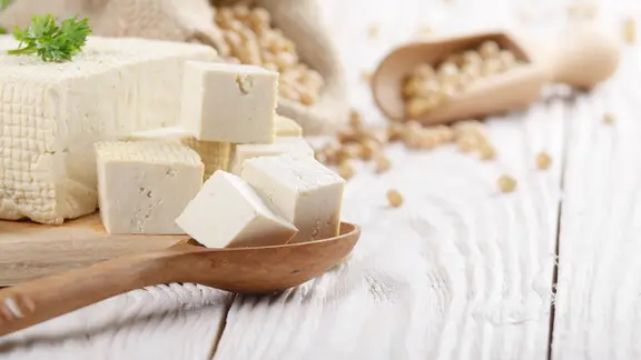 Soy Bean curd tofu on cutting board and in hemp sack on white wooden kitchen table. Space for text