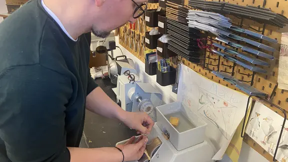 Ein Mann steht an einer Schleifmaschine und schleift ein Brillenglas