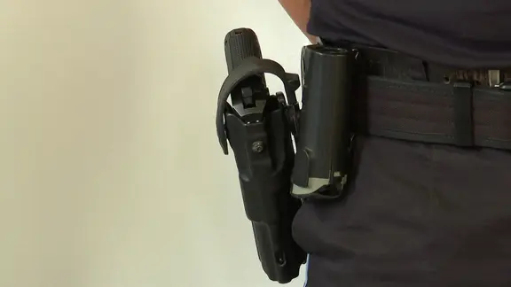 Nahaufnahme eines am Gürtel getragenen Holsters mit einer Pistole an einer dunkelblauen Dienstkleidung.