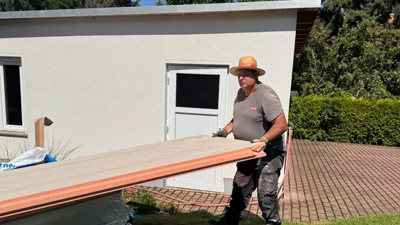 Ein Mann mit Strohhut trägt ein Dachteil.