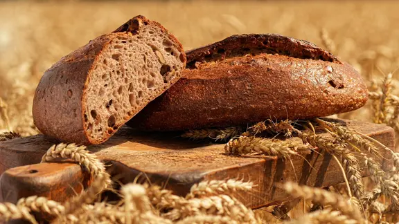 Ein aufgeschnittenes Brot liegt auf einem Brett in einem Getreidefeld