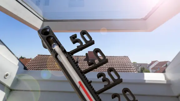 Thermometer vor einem Dachfenster zeigt heiße Raumtemperatur an.