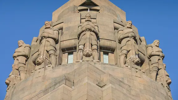 Ritterfiguren an der Kuppel des Völkerschlachtdenkmals. Die Krieger stehen frontal und breitbeinig, gestützt auf ihre Schwerter.