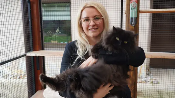  Kristin Vogel hält ihren Kater Artus auf dem Arm und lächelt in die Kamera. 

