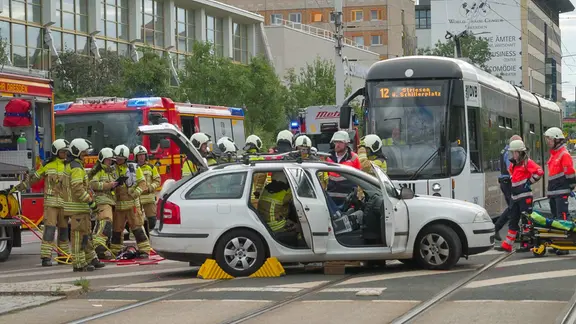 PKW steht nach Zusamnenstoß mit Straßenbahn auf den Schienen, dahinter Einstatzkräfte von Feuerwehr und Rettung