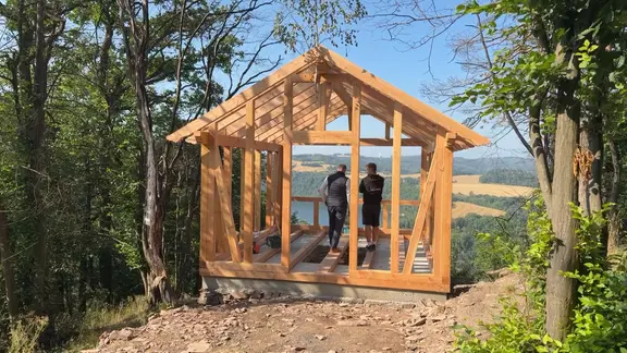 Zwei Männer stehen in einer Holzhütte.