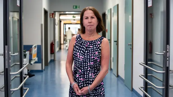 Eine Frau steht in einem Gang in einem Krankenhaus und schaut in die Kamera