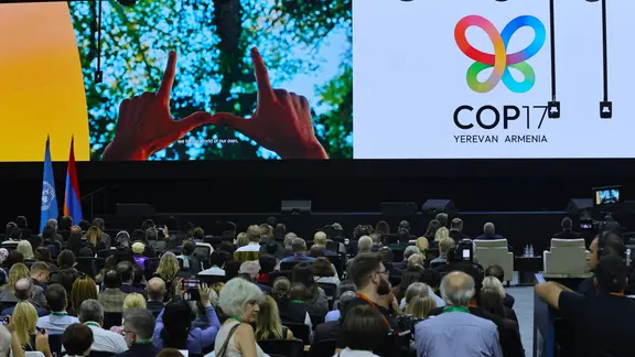 Eine Konferenzhalle, in der viele Menschen sitzen, im Hintergrund eine große Gra