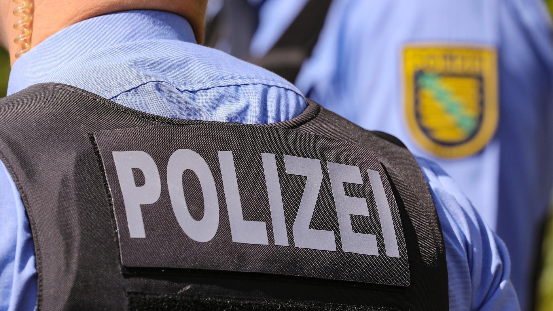 Aufschrift Polizei auf Polizeiweste im Anschnitt. Im Bildhintergrund das Landeswappen Polizei Sachsen in der Bildunschärfe. | picture alliance/dpa/dpa-Zentralbild | Tino Plunert