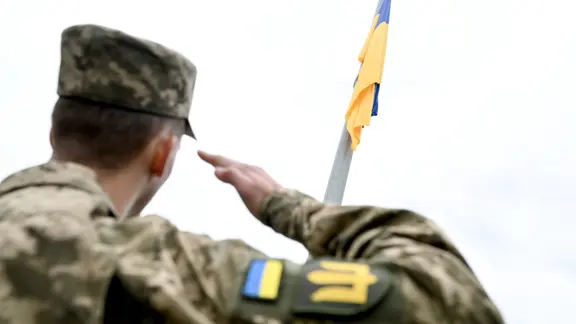 Ein ukrainischer Soldat salutiert vor der ukrainischen Flagge.