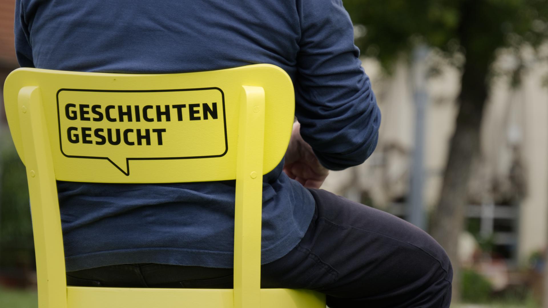 Auf der Lehne eines gelben Stuhls steht 