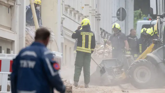 Einsatzkräfte der Feuerwehr und des Technischen Hilfswerks arbeiten sich durch Trümmerteile eines eingestürzten Hauses. 