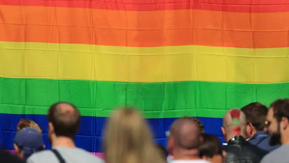Menschen stehen vor einer riesigen Regenbogenflagge.