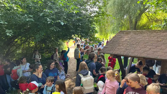 Viele Kinder und einige Erwachsene im Grünen, zwischen ihnen ein Unterstand