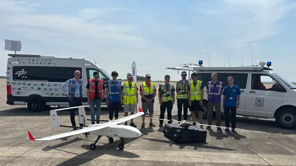 Mehrere Personen betrachten eine Drohne auf einer planen Fläche.