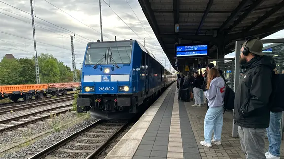 Eine blaue Lok fährt in den Weimarer Bahnhof ein, am Bahnsteig stehen Fahrgäste