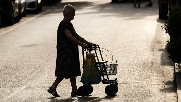 Ältere Frau mit Rollator bei Sommerhitze allein in der Stadt unterwegs