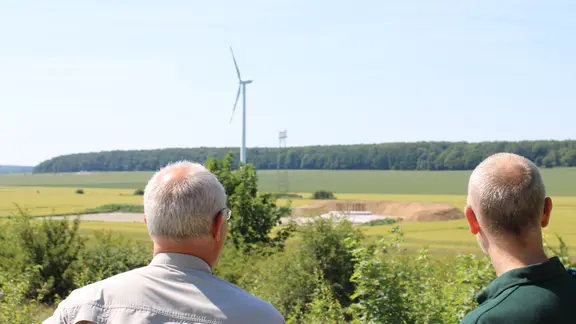 Jörn Ripken und Kollege Gerd Thomsen mit Blick auf Windräder vor dem Wald. 