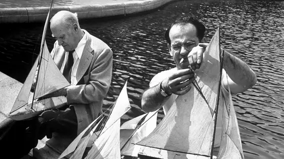 Lyonel Feininger (αριστερά), επισκευάζει μοντέλο ιστιοφόρου | Εικόνες IMAGO/Pond5 Lyonel Feininger (αριστερά), επισκευάζοντας ένα μοντέλο ιστιοφόρου. Μια ασπρόμαυρη φωτογραφία, ο Feininger κάθεται με ένα ελαφρύ κοστούμι δίπλα σε έναν άλλο άνδρα, υπάρχει νερό πίσω του