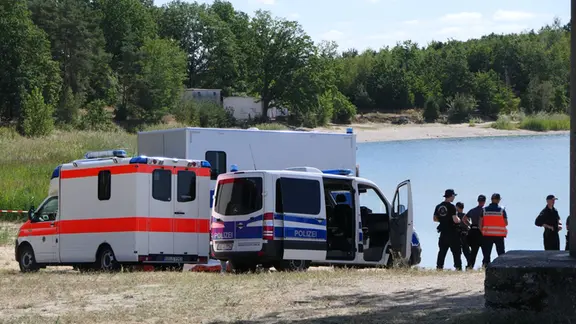 Einsatzkräfte stehen an einem See. 