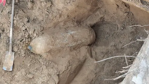 Eine langer, zylindrischer Gegenstand liegt ausgegraben in einem Erdloch.