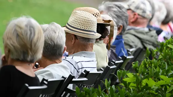 Ältere Menschen besuchen in einem Kurpark das Konzert eines Schulorchesters.