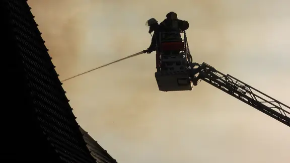 Feuerwehrleute mit Leiterwagen auf einer ausgefahrenen Drehleiter beim einem Dachstuhlbrand