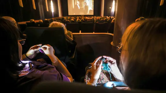 Blick über mehrere Kino-Sitze, in denen Menschen stricken.