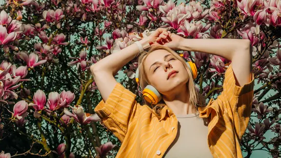 Eine Frau in einem gelben Hemd, die mit Kopfhörern zwischen blühenden Magnolienbäumen Musik genießt