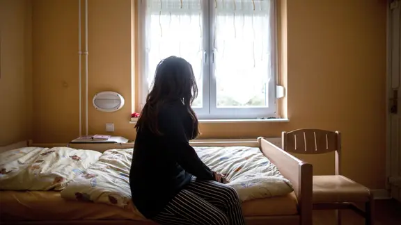 Eine Frau sitzt in einem Frauenhaus auf einem Bett. 