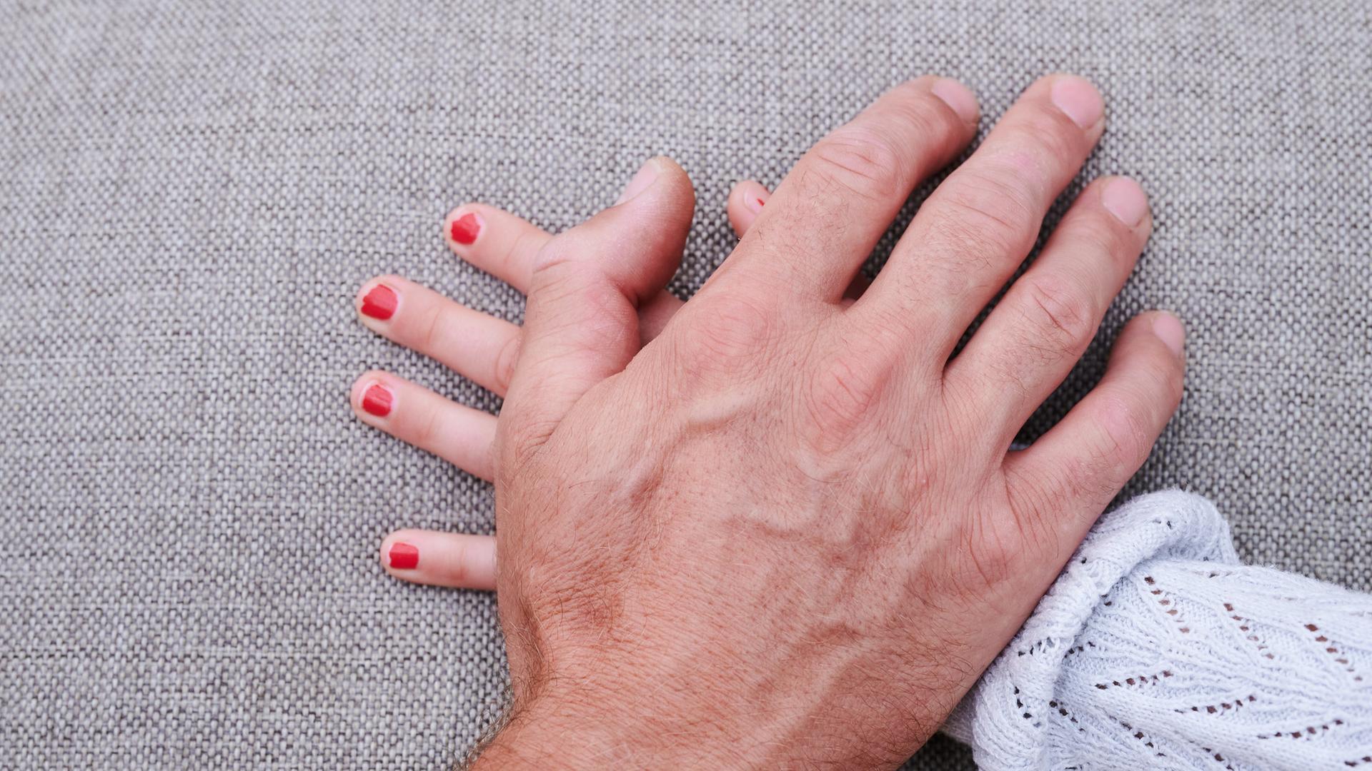 Eine Männerhand liegt auf einer Mädchenhand | dpa/Annette Riedl