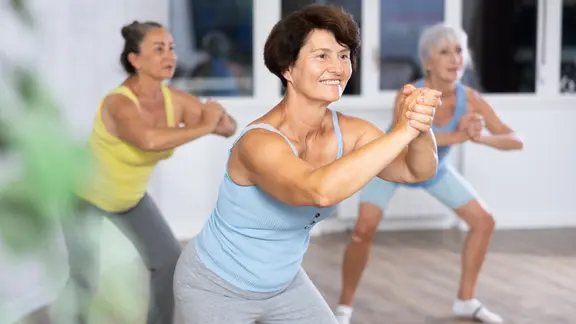Gruppe älterer Frauen übt Tanzschritte im Fitnessstudio.