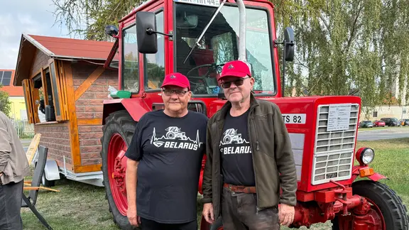 Zwei ältere Männer stehen vor einem roten Traktor.