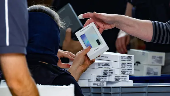 Ein Polizist mit Sturmhaube steht vor einer Ladesfläche auf dem Handy-Verpackungen liegen.