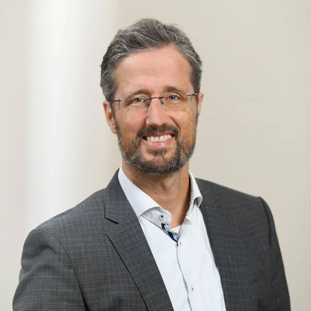 Porträt von lächelndem Mann mit kürzeren Haaren,  Brille und Bart in Anzug