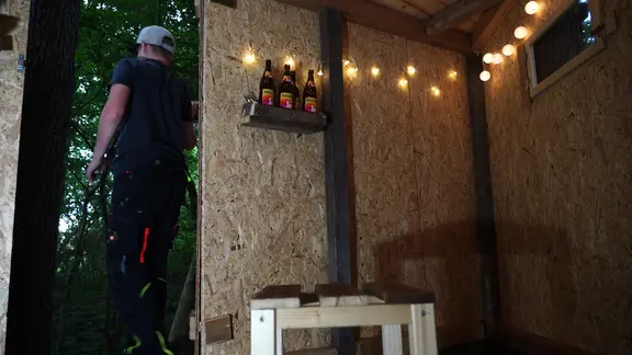 Das Innere des Baumhauses mit Stuhl, Fenster, Lichterkette und Getränkehalterung