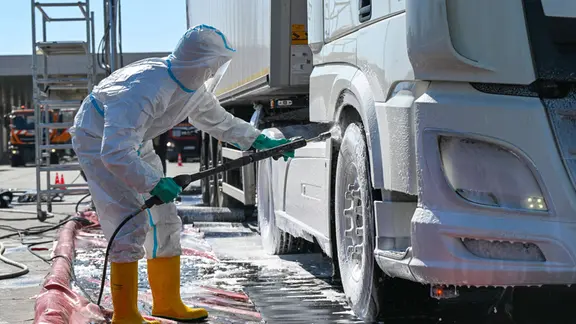 Ein Mitarbeiter in Schutzkleidung desinfinziert die Reifen eines Trucks.