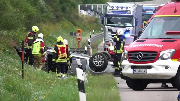Neben der A4 liegt ein silbernes Auto auf dem Dach. Davor stehen Feuerwehrleute.