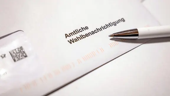 Ein Schreiben mit der Aufschrift „Amtliche Wahlbenachrichtigung“ liegt auf einem Tisch, daneben ein Kugelschreiber. 