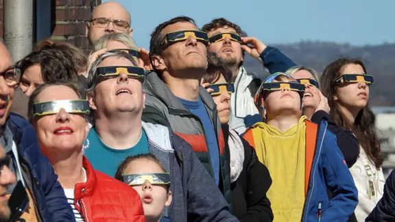 Menschen mit Schutzbrillen blicken in den Himmel.