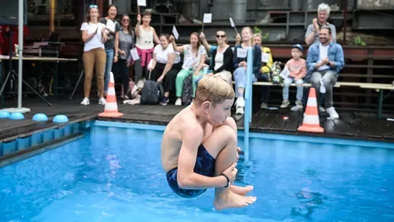 Ein Junge springt mit angezogenen Beinen ins Wasser