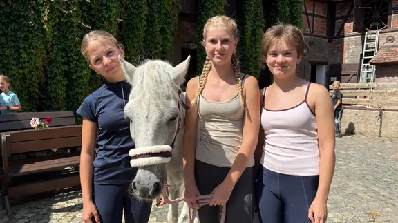 Drei Mädchen stehen neben einem weißen Pony.