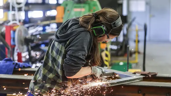 Eine Auszubildende zum Metallbauer arbeitet mit einem Schleifgerät. 