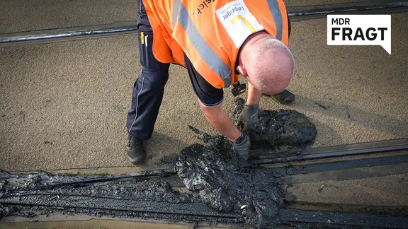 Ein Mitarbeiter der LVB bückt sich, um die Schienen reinigen. 