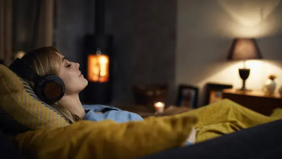 Lächelnde Frau hört Musik auf dem Sofa.