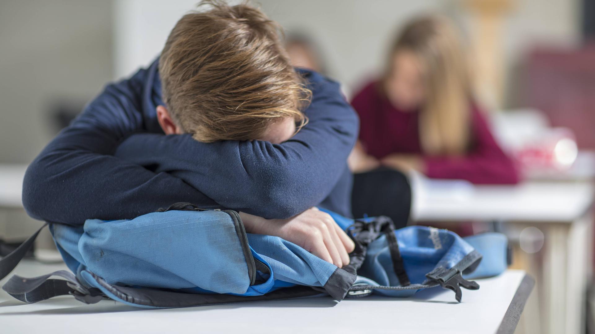 Ein Teenager schläft im Unterricht und hat seinen Kopf auf dem Tisch abgestützt. | IMAGO / Westend61