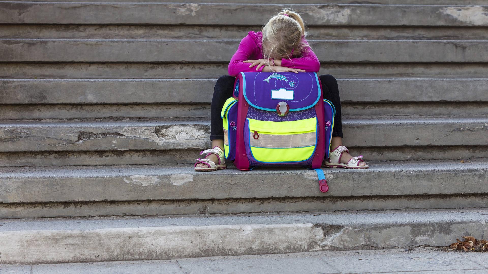 Trauriges Mädchen mit Schulranzen, das auf einer Treppe sitzt. | IMAGO / Westend61
