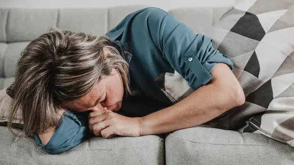 Eine Frau liegt zusammengekrümmt auf einer Couch.